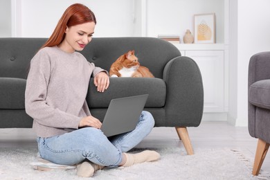 Photo of Woman working with laptop near cat on sofa at home