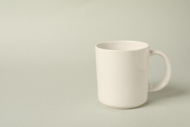 Photo of One white ceramic mug on light grey background, space for text