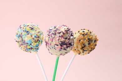 Photo of Sweet cake pops decorated with sprinkles on pale pink background, closeup. Delicious confectionery