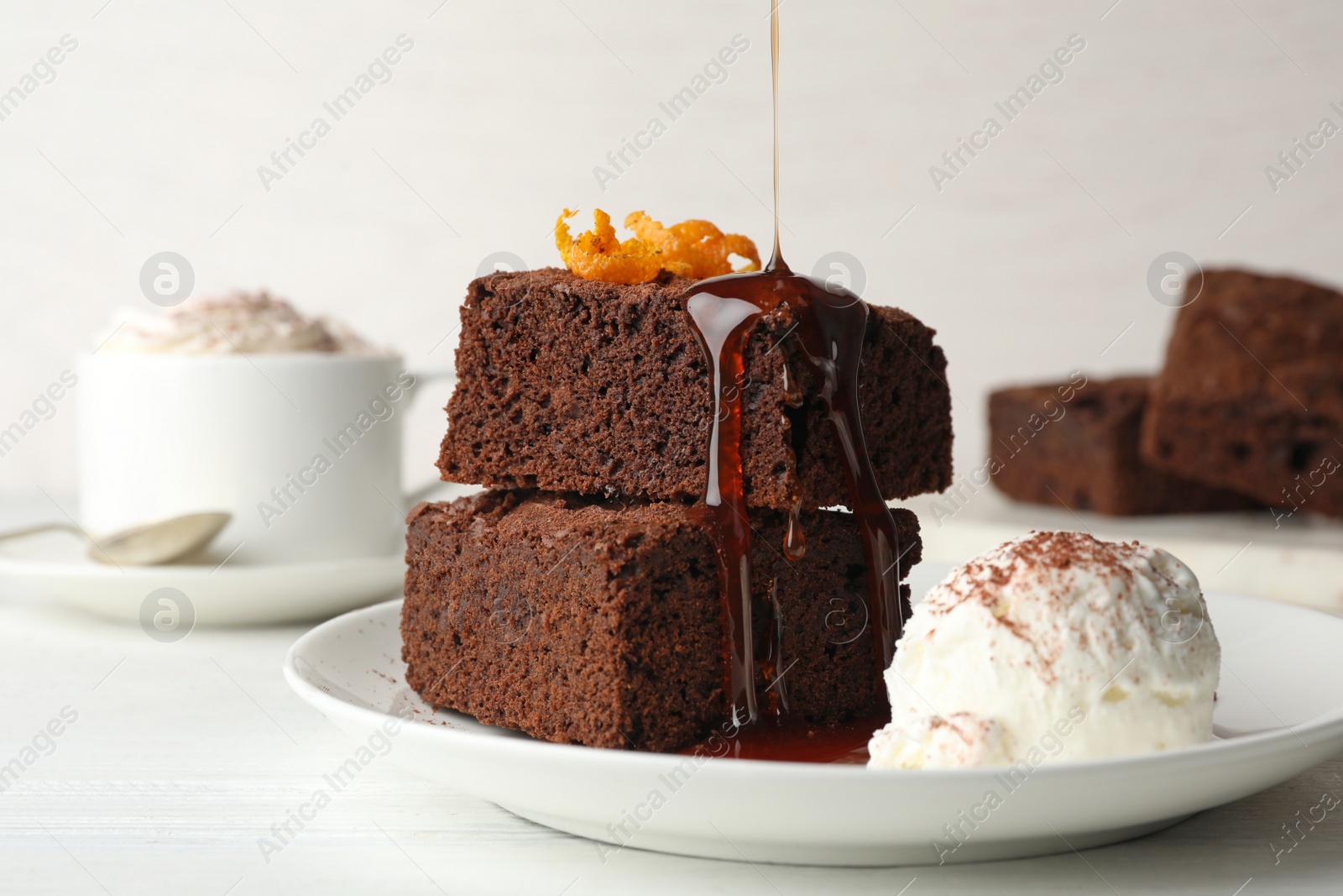 Photo of Pouring sauce onto fresh brownies served with ice-cream on plate. Delicious chocolate pie