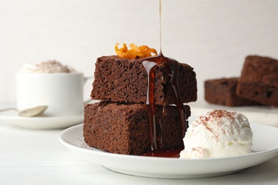 Pouring sauce onto fresh brownies served with ice-cream on plate. Delicious chocolate pie
