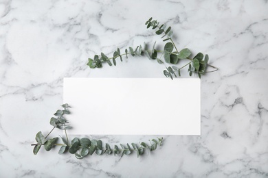 Photo of Fresh eucalyptus leaves and blank card with space for design on marble background, top view