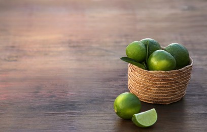 Photo of Fresh ripe limes and wicker basket on wooden table. Space for text
