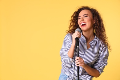 Photo of Portrait of curly African-American woman singing in microphone on color background. Space for text