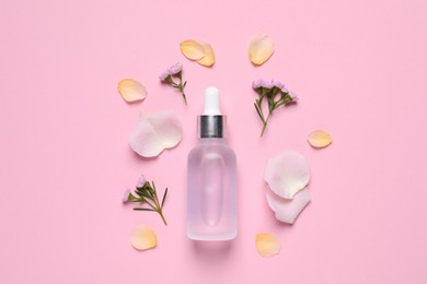 Bottle of cosmetic serum, flowers and petals on pink background, flat lay