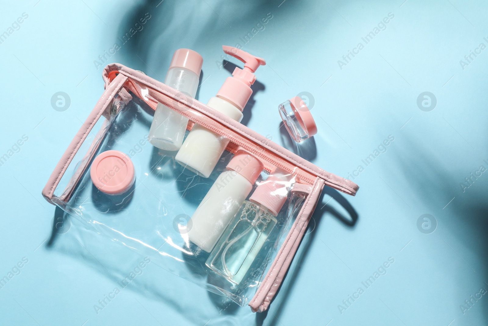 Photo of Cosmetic travel kit with plastic bag on light blue background, top view. Space for text