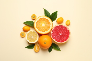 Photo of Fresh juicy citrus fruits with green leaves on beige background, flat lay