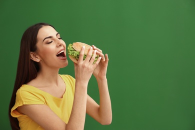 Photo of Young woman eating tasty burger on color background. Space for text