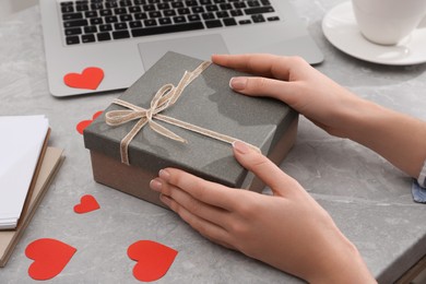 Photo of Woman with gift box at light grey marble table, closeup. Valentine's day celebration