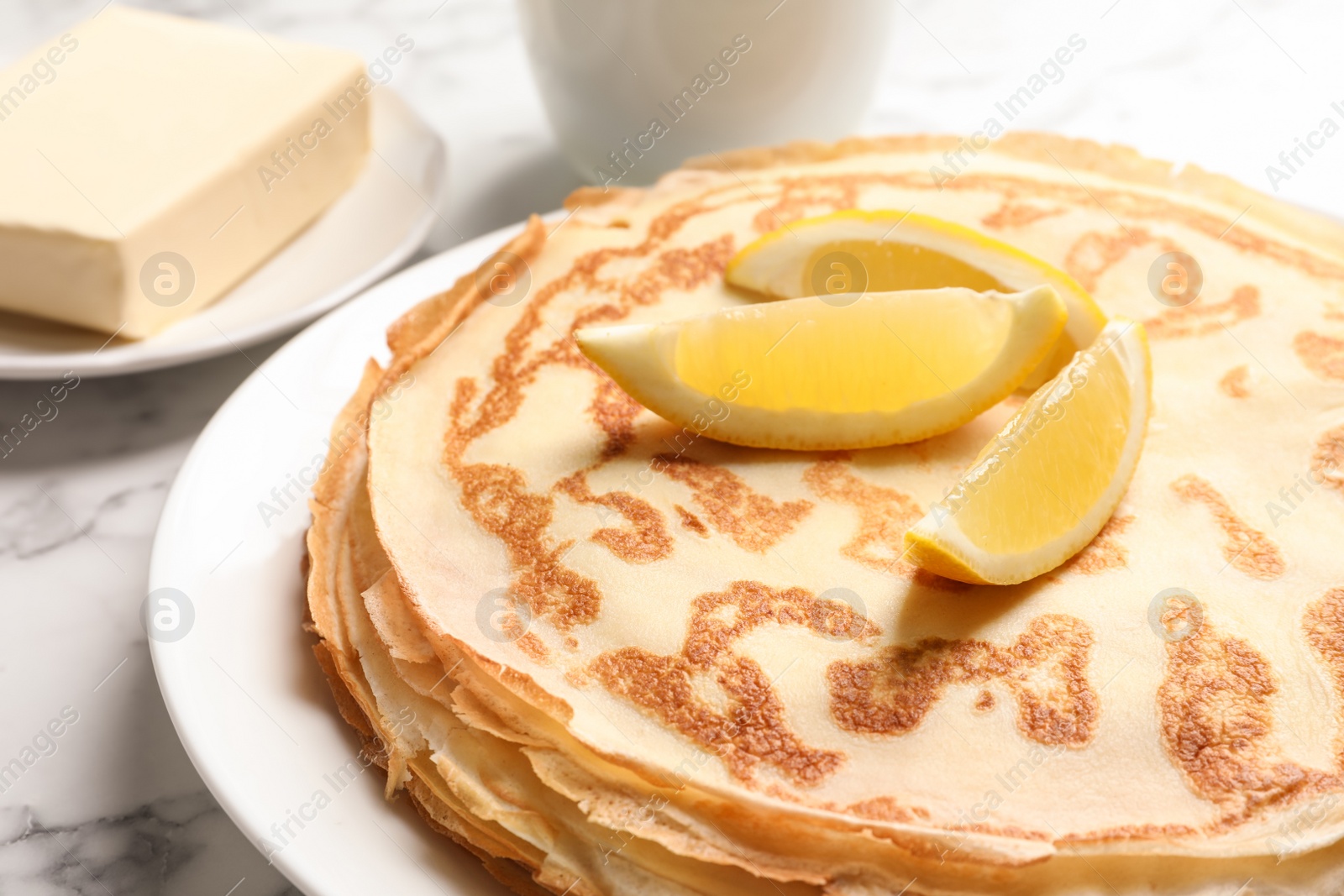 Photo of Thin pancakes served with lemon on plate, closeup