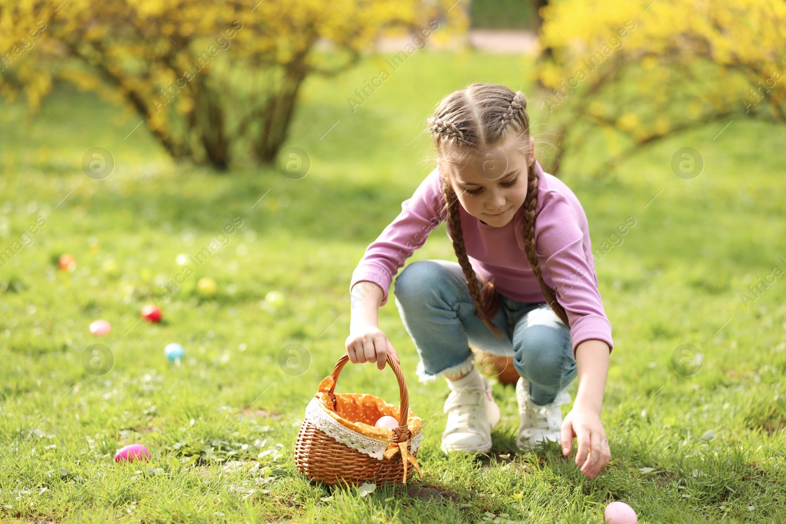 Photo of Easter celebration. Cute little girl hunting eggs outdoors, space for text