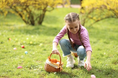 Photo of Easter celebration. Cute little girl hunting eggs outdoors, space for text