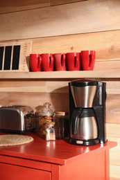 Photo of Modern coffeemaker on red table near wooden wall