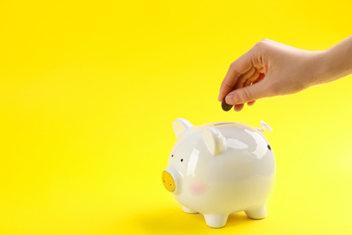 Photo of Woman putting coin into piggy bank on yellow background, closeup. Space for text