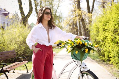 Beautiful woman with bicycle and bouquet of yellow tulips outdoors on sunny spring day