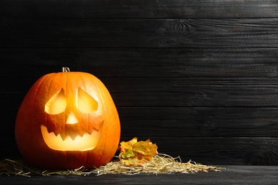 Photo of Pumpkin jack o'lantern, straw and autumn leaves on black wooden table, space for text. Halloween decor