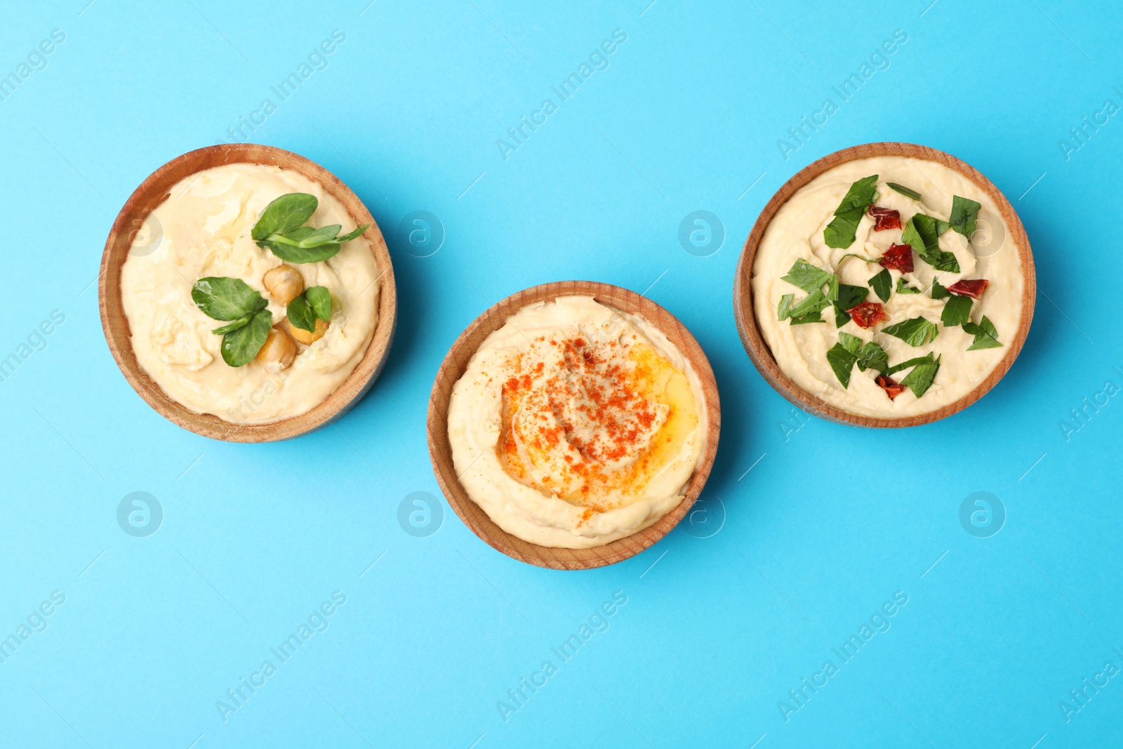 Photo of Different kinds of tasty hummus in bowls on light blue background, flat lay