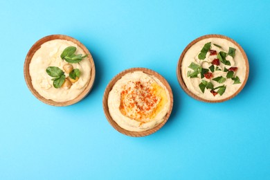 Photo of Different kinds of tasty hummus in bowls on light blue background, flat lay