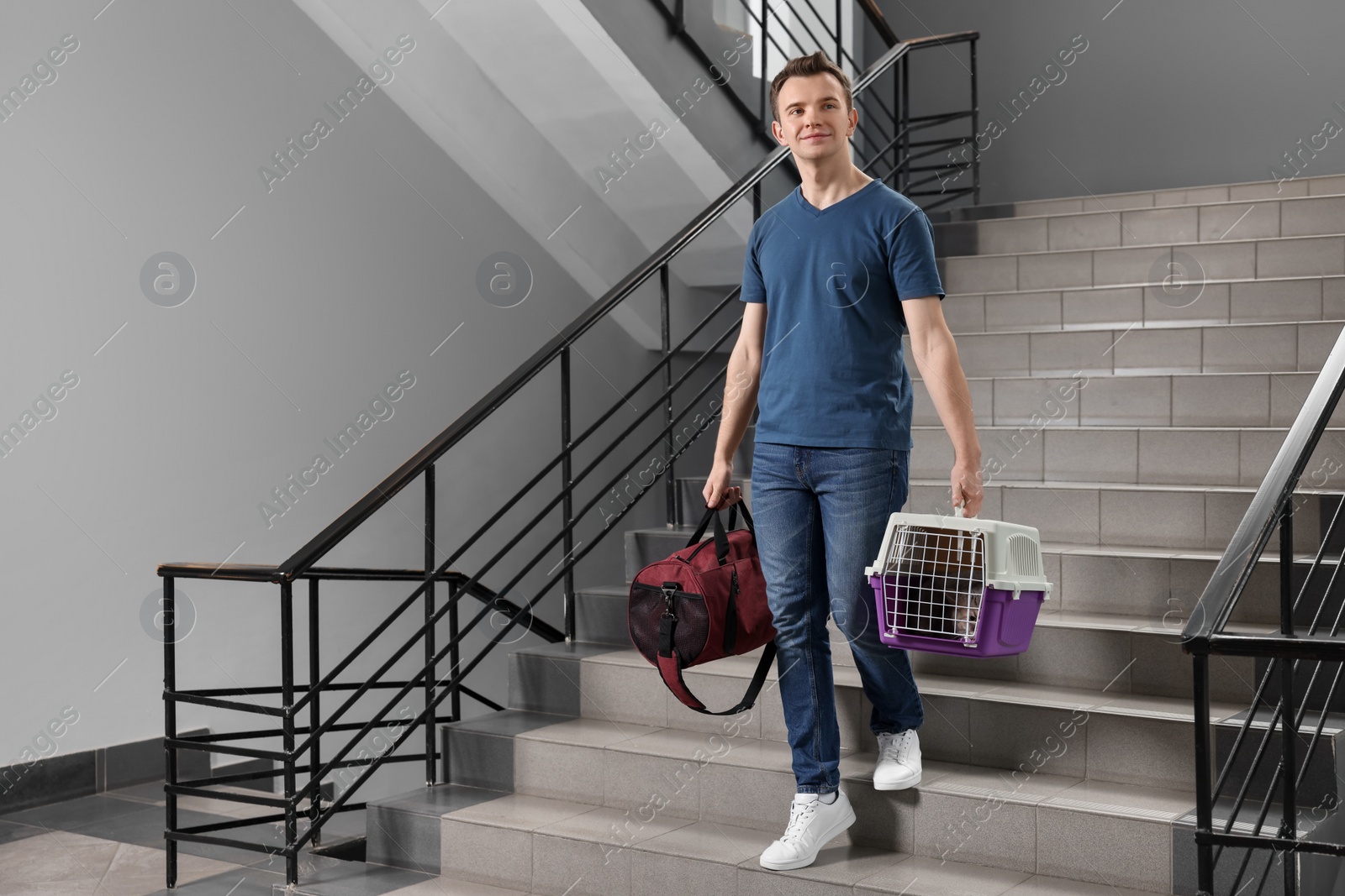 Photo of Travel with pet. Man holding carrier with cute cat and bag on stairs indoors