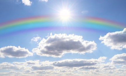 Image of Beautiful rainbow in blue sky with white clouds on sunny day