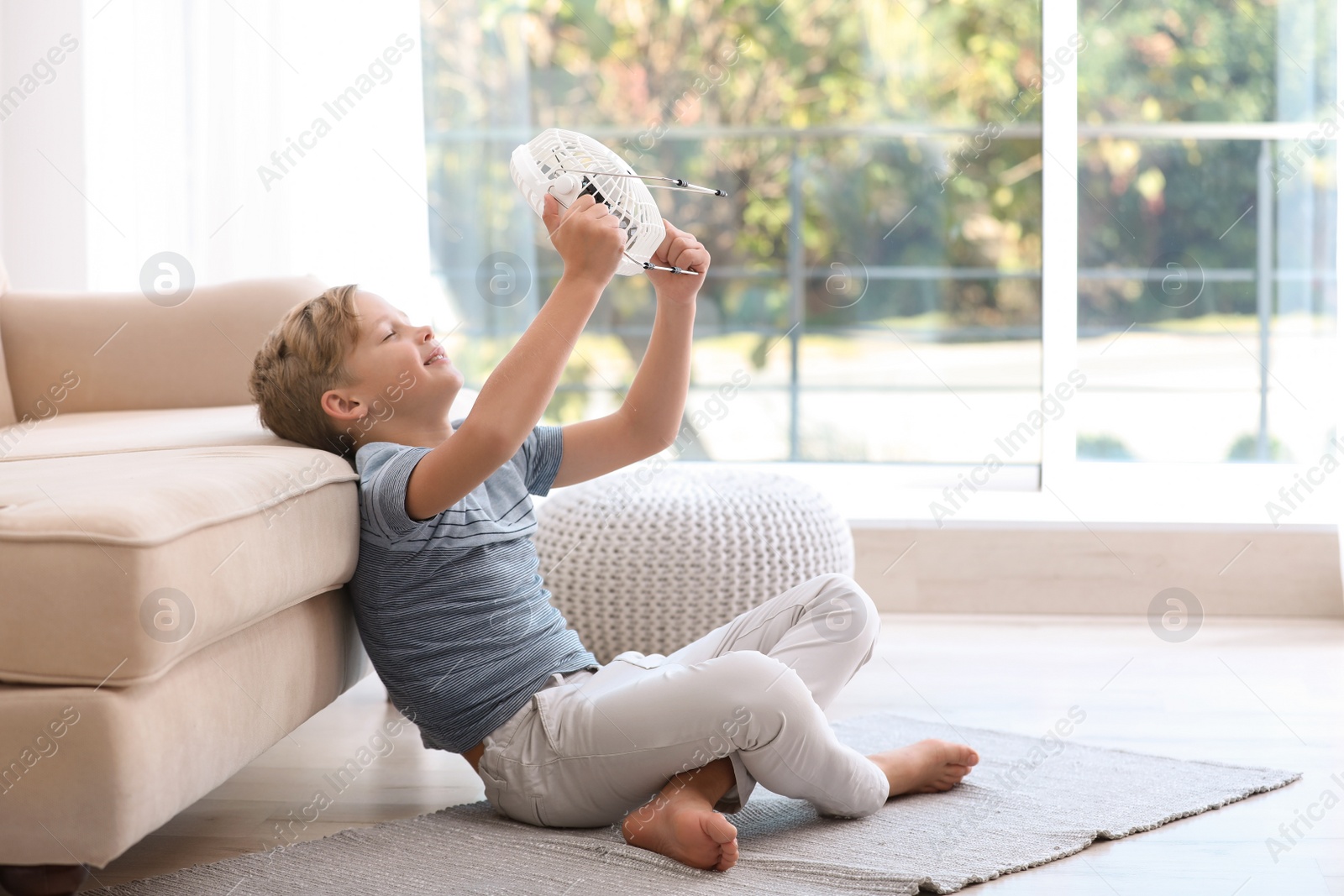 Photo of Little boy with fan relaxing at home. Summer heat