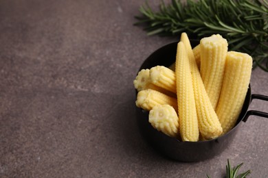 Tasty fresh yellow baby corns in dish on brown table, above view