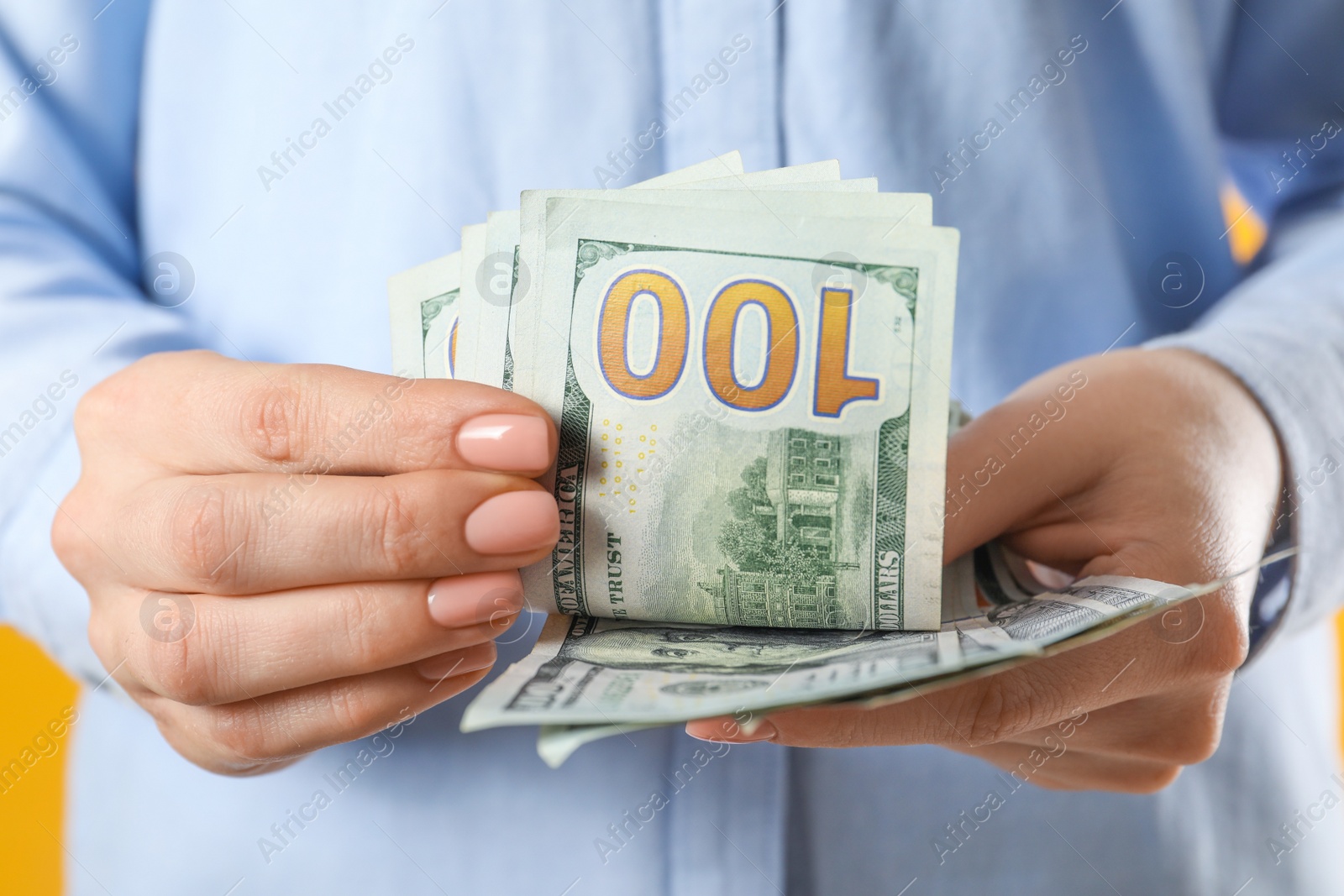 Photo of Woman counting dollar banknotes on yellow background, closeup. Money exchange concept