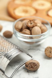 Photo of Nutmeg seeds and grater on white marble table, closeup