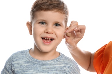 Mature woman putting hearing aid in little grandson's ear on white background, closeup