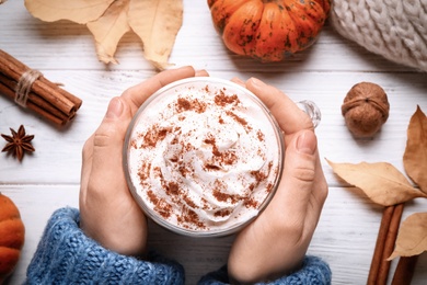 Photo of Woman holding tasty pumpkin latte at white wooden table, top view