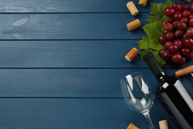 Tasty red wine and grapes on blue wooden table, flat lay. Space for text