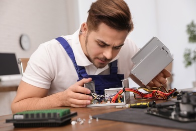 Photo of Male technician repairing power supply unit at table indoors