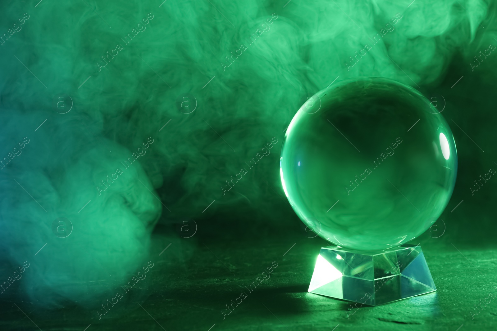 Photo of Crystal ball on table and smoke against dark background, space for text. Predictions of future