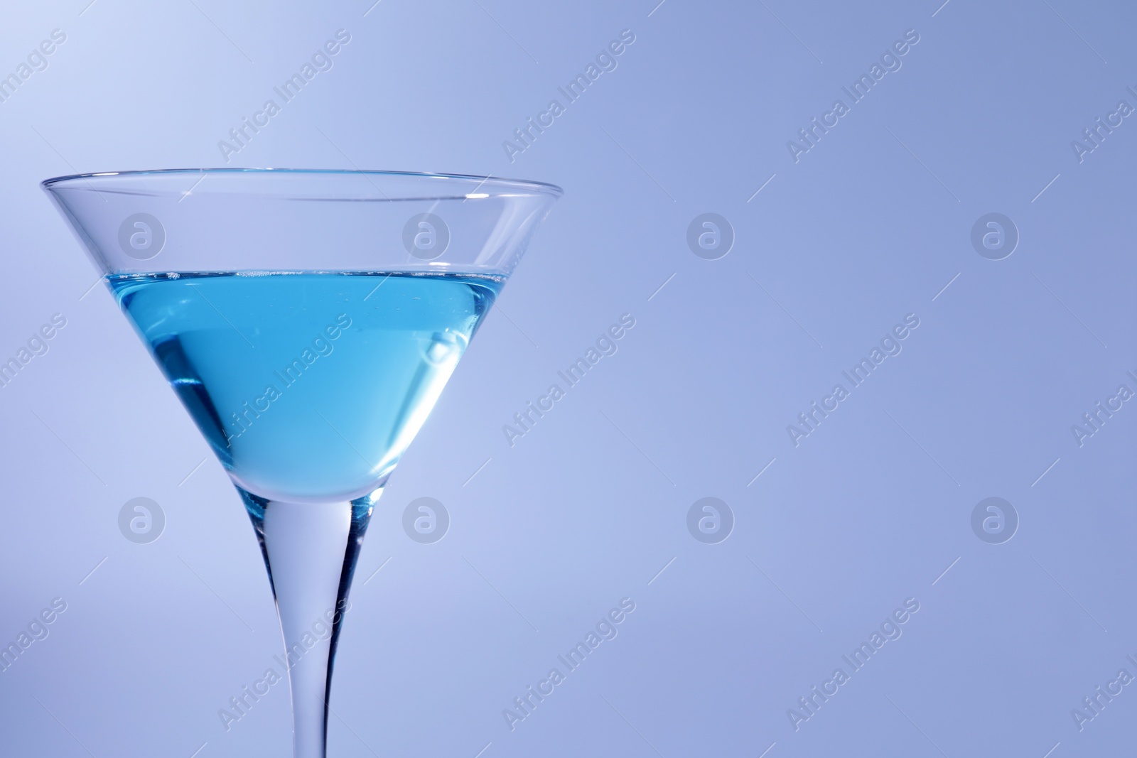 Photo of Martini glass with delicious cocktail on light blue background, space for text