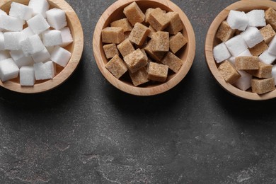 Photo of Different sugar cubes in bowls on gray textured table, flat lay. Space for text