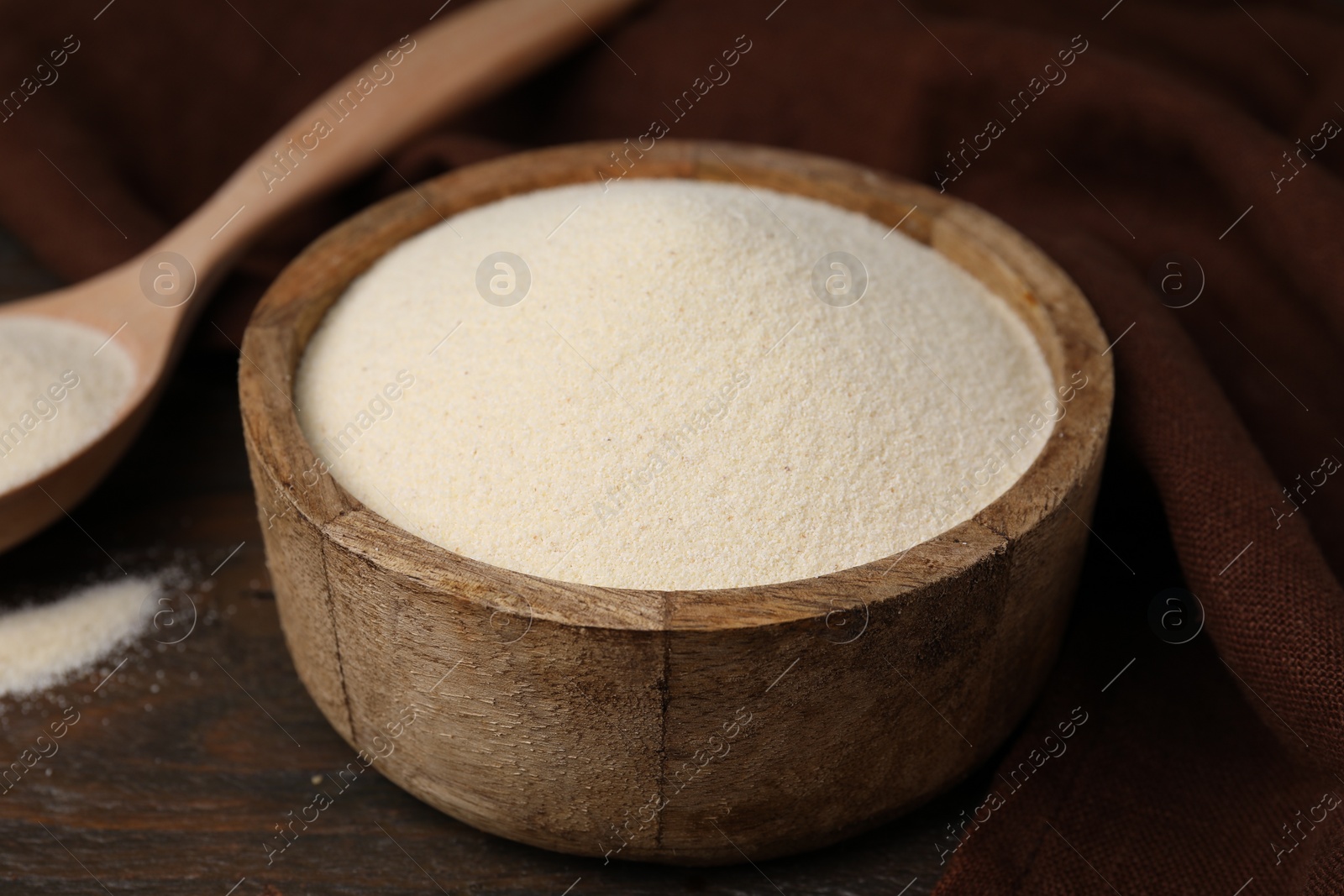 Photo of Uncooked organic semolina in bowl and spoon on wooden table, closeup