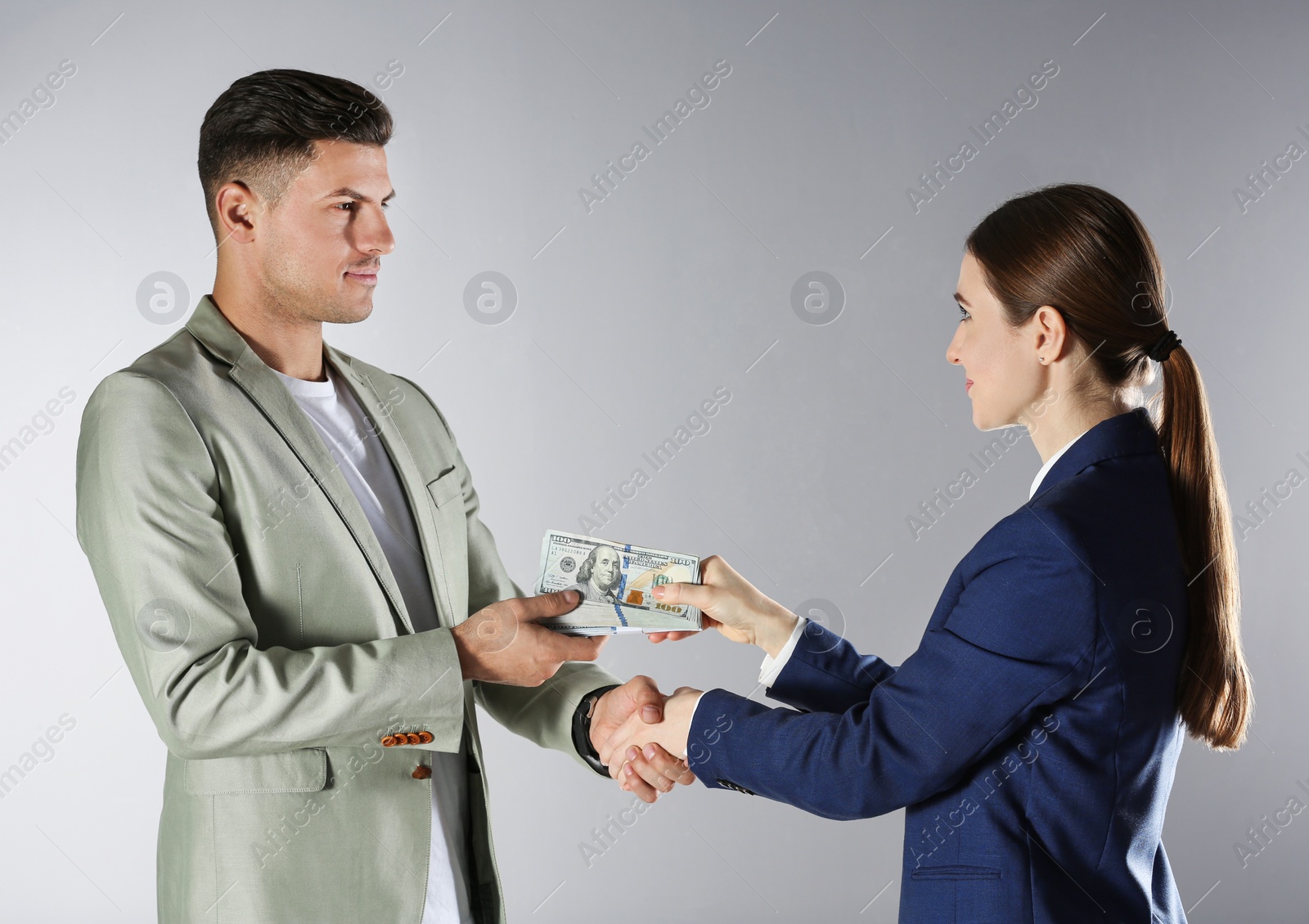 Photo of Woman shaking hands with man and offering bribe on grey background