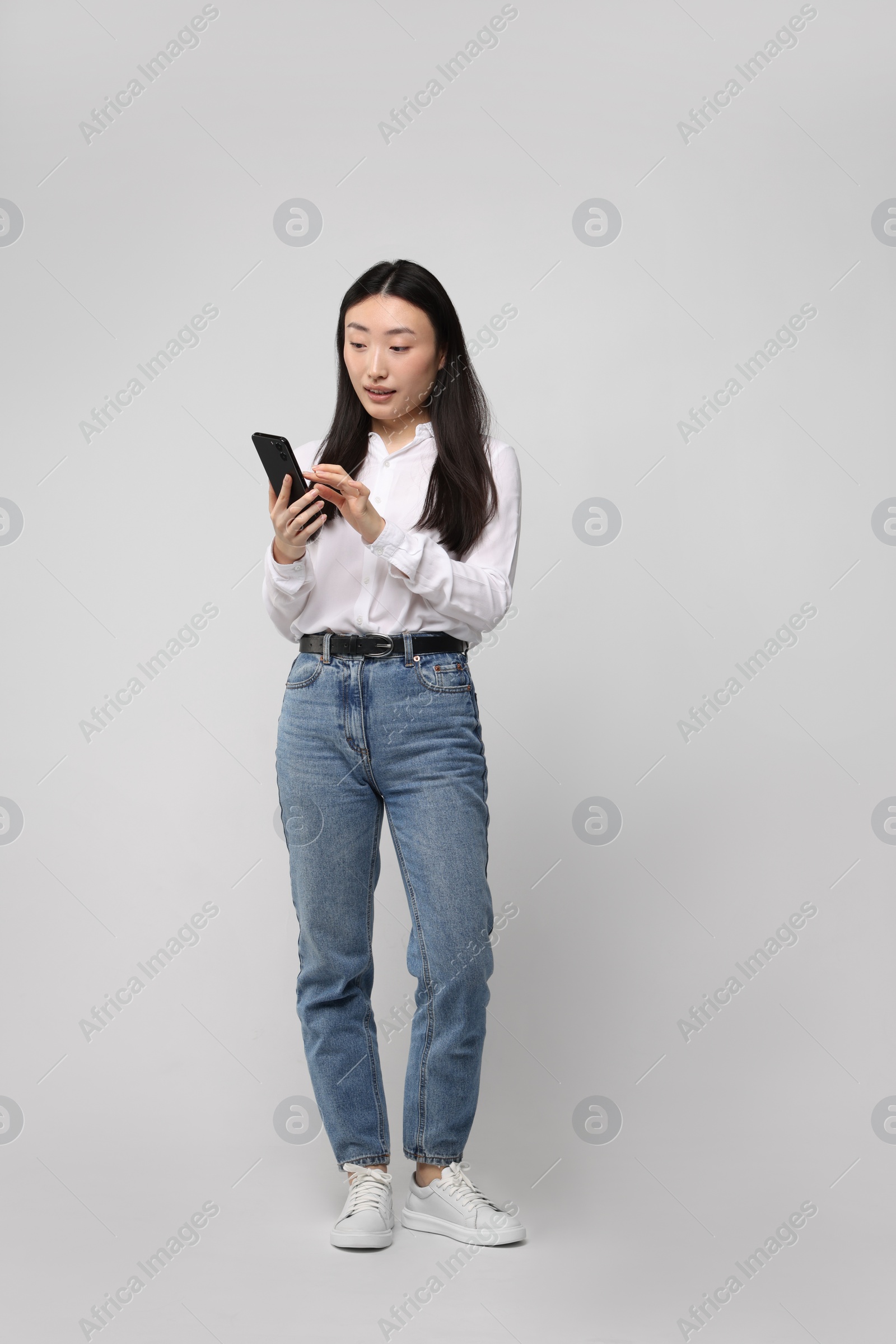 Photo of Full length portrait of beautiful woman with smartphone on light background