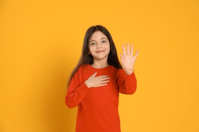 Happy little girl waving to say hello on yellow background