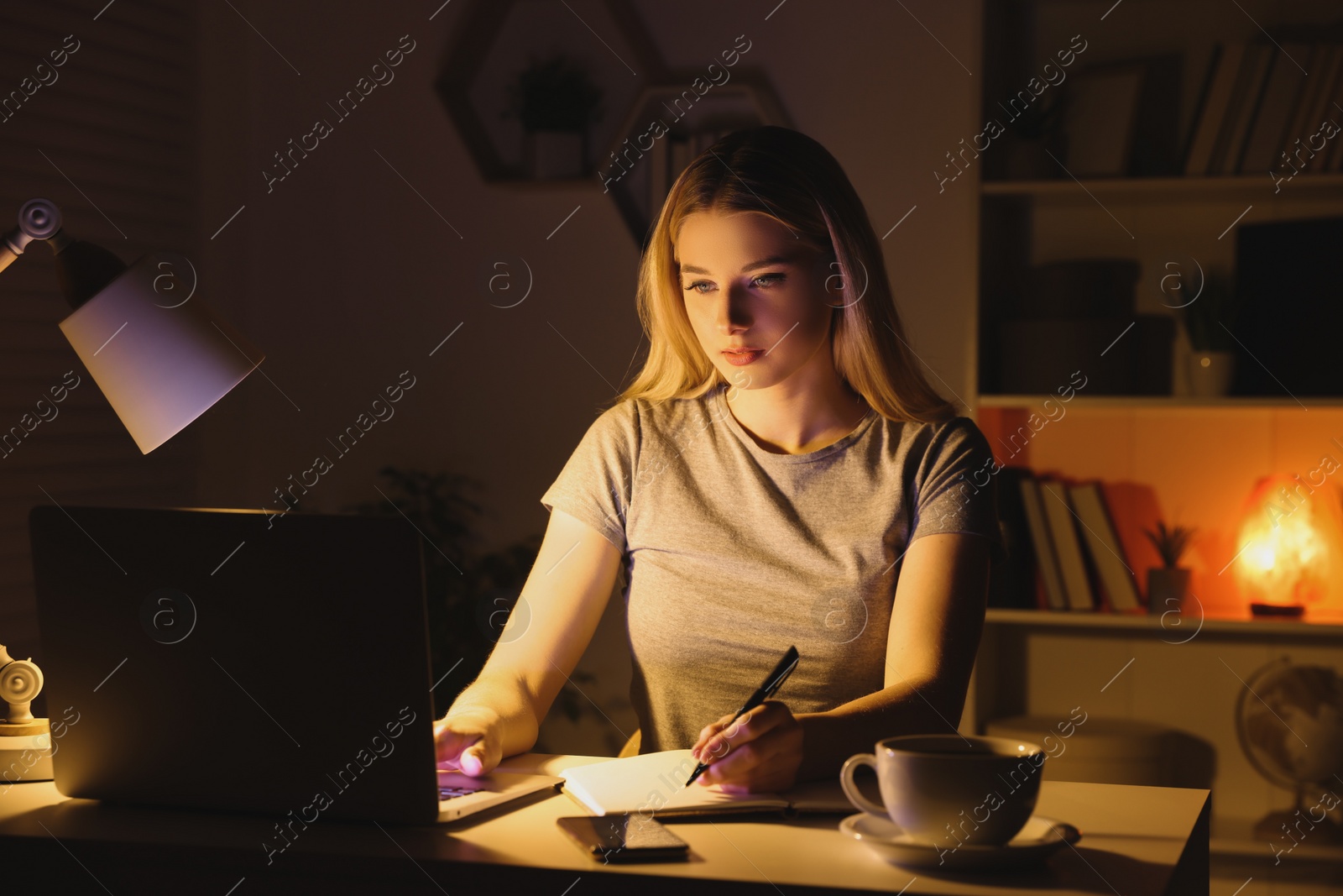 Photo of Home workplace. Woman with pen and notebook working on laptop at white desk in room