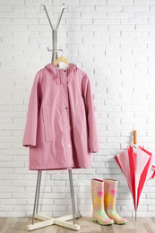 Photo of Umbrella, raincoat and rubber boots near white brick wall