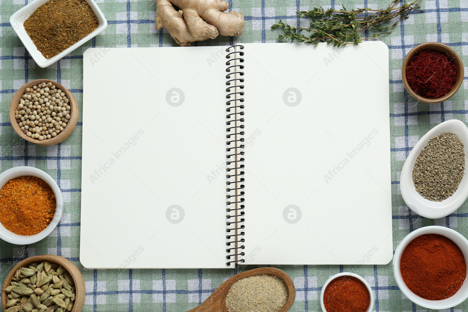 Photo of Blank recipe book surrounded by different ingredients on checkered tablecloth, flat lay. Space for text