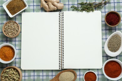 Blank recipe book surrounded by different ingredients on checkered tablecloth, flat lay. Space for text