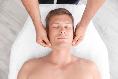 Relaxed man receiving head massage in wellness center, top view