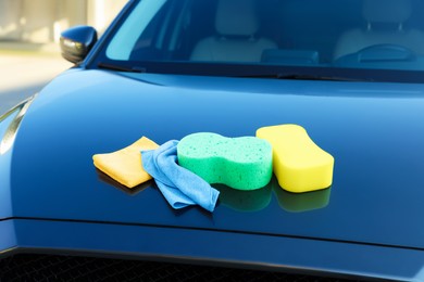 Photo of Sponges and rags on car hood outdoors. Cleaning products