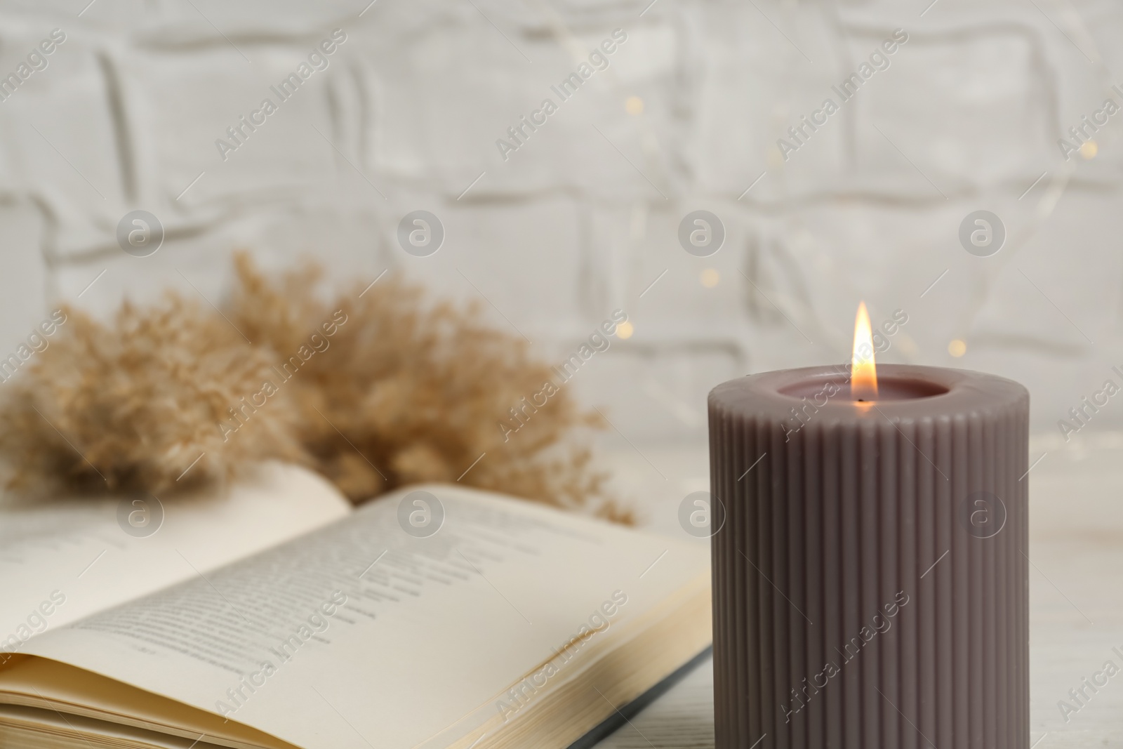 Photo of Burning candle and open book on table, space for text