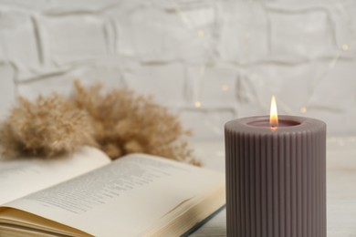 Burning candle and open book on table, space for text