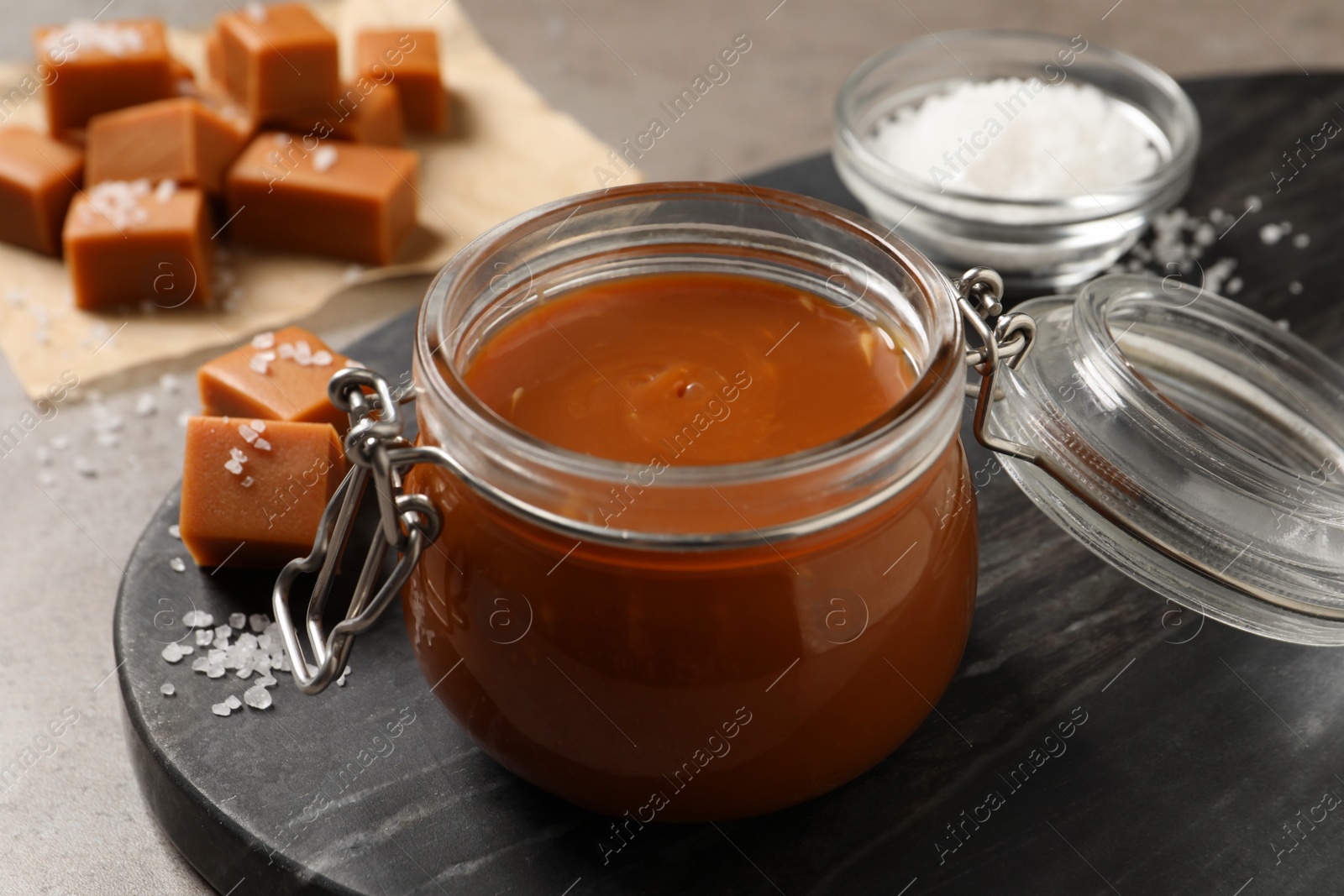 Photo of Tasty salted caramel in glass jar on grey table, closeup