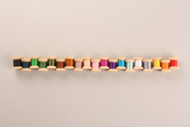 Photo of Different colorful sewing threads on light grey background, flat lay