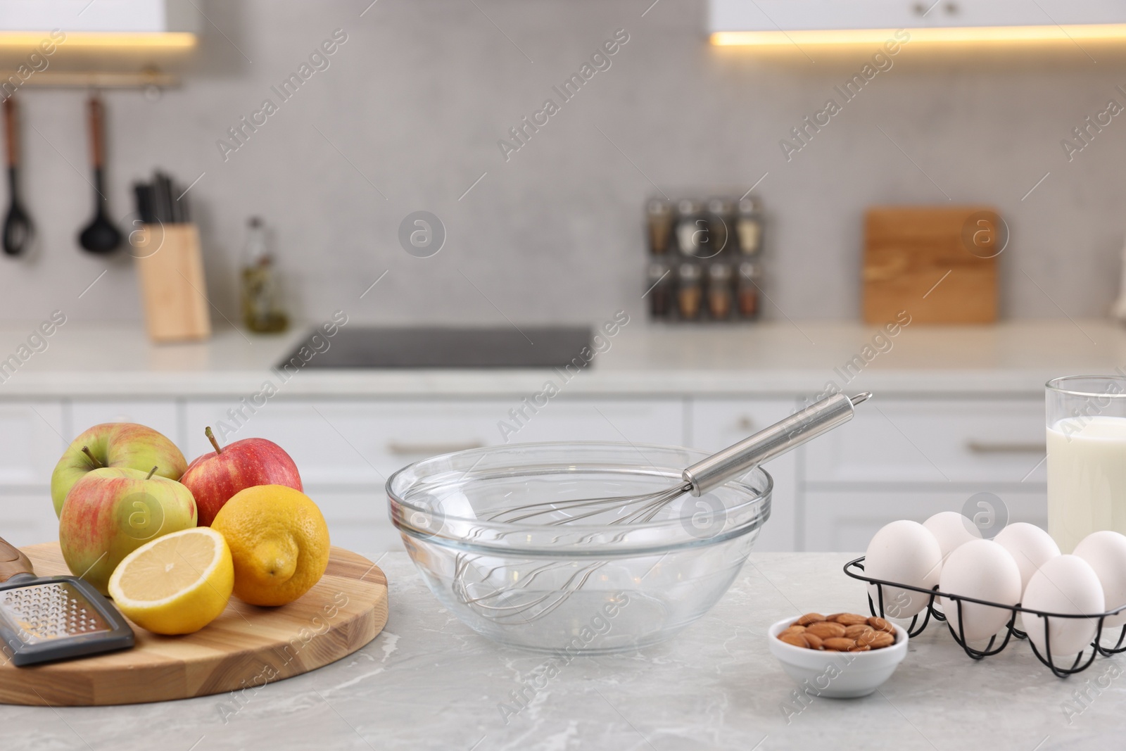 Photo of Metal whisk, bowl, grater and different products on gray marble table in kitchen